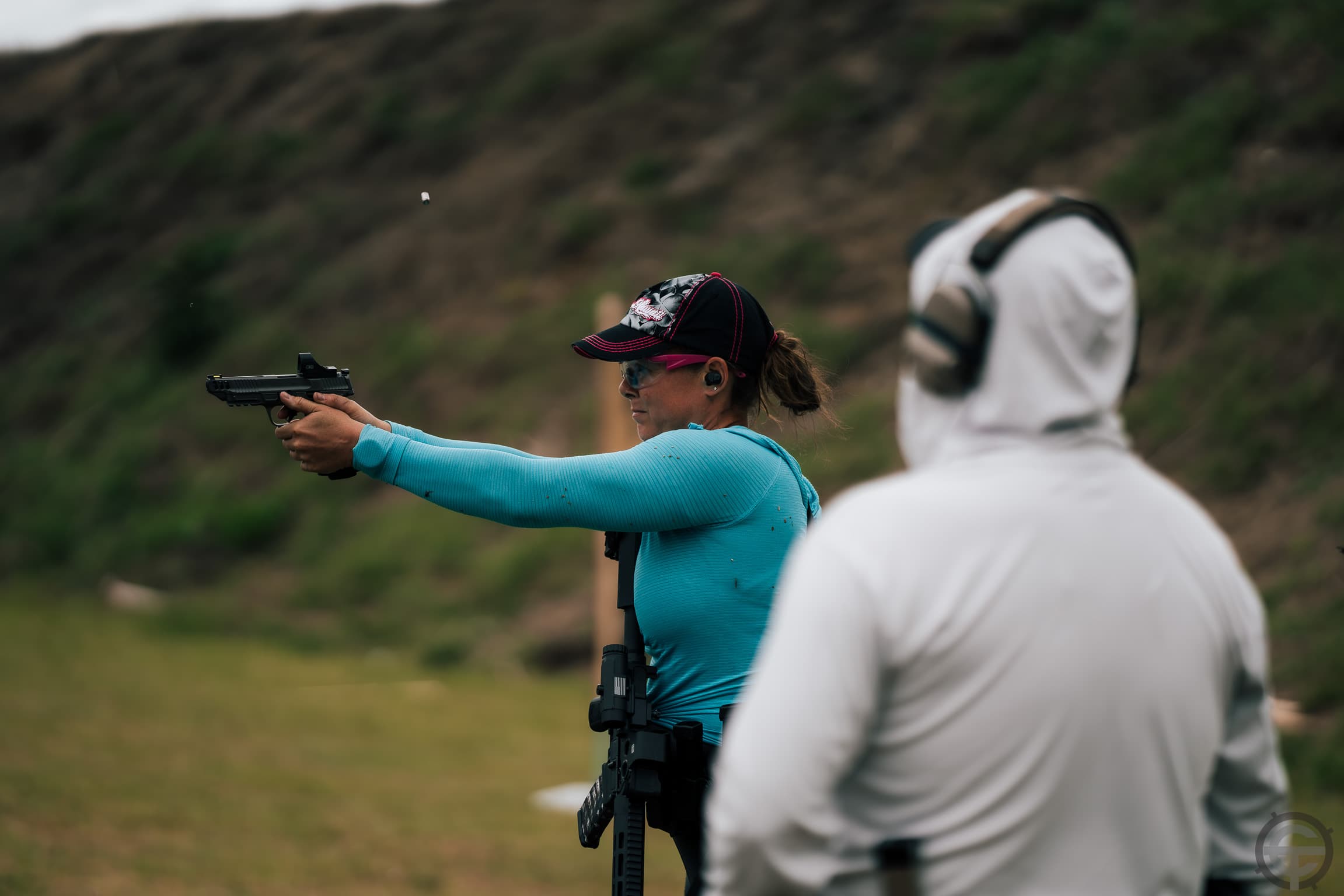 Student firing pistol with shell mid-eject while instructor observes